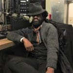 black man wearing a hat slumped in a chair in front of microphone