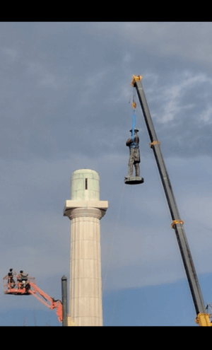 statue being taken off a pedestal with a crane