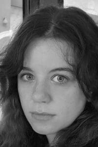 Black and white image of a young caucasian woman with dark hair and light eyes against a nondescript background.