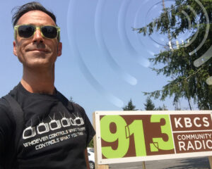 guy in black tshirt outside in front of 913 kbcs sign some radar waves graphic