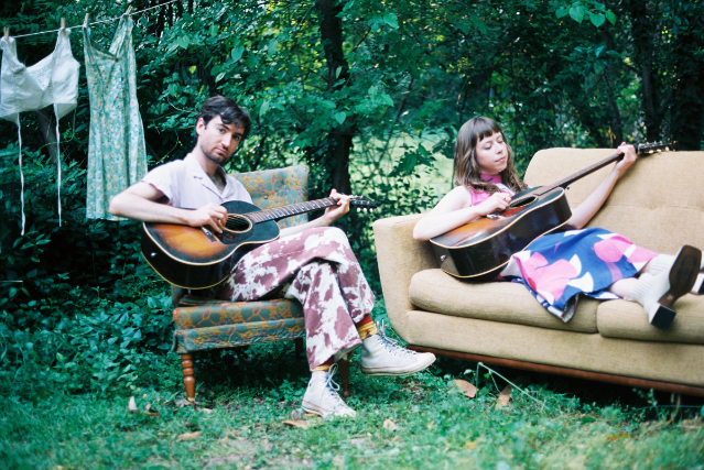 two people sitting on a couch with guitars.