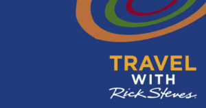 The image is a logo for the program “Travel with Rick Steves.” The background is a deep blue color. At the top, there are three curved lines in red, green, and brown, resembling stylized travel paths or trails, forming an abstract, circular pattern. Below these lines, the text “TRAVEL WITH Rick Steves” is prominently displayed. The word “TRAVEL” is in bold, uppercase yellow letters. The word “WITH” is in smaller, bold, uppercase white letters underneath “TRAVEL.” Below “WITH,” the name “Rick Steves” is written in a white, cursive font that resembles a signature. The overall design is clean and modern, with the curved lines adding a dynamic, travel-oriented feel to the logo. The text is clear and easy to read, with the deep blue background providing strong contrast.