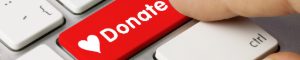 The image shows a red keyboard key labeled “Donate” with a heart symbol next to it. A finger is poised to press the key. This image serves as a button; clicking it will take you to the KBCS Donate page at https://www.kbcs.fm/donate/.