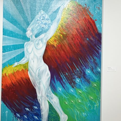 The attached image features a colorful and vibrant painting that depicts a powerful, ethereal figure. The figure, set against a radiant background of blue, green, red, and orange hues, appears to be floating or in mid-motion, with one arm outstretched. The figure’s body is rendered in a semi-transparent, glowing white with geometric patterns on the head, suggesting a sense of otherworldliness or transcendence. The vibrant colors and dynamic brushstrokes evoke a feeling of energy and freedom, while the composition blends elements of the surreal with abstract expression. The painting radiates a sense of movement, empowerment, and the blending of nature with the human form.