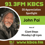 A KBCS DJ appreciation poster with an image of John Pai, the host of Giant Steps. He is an asian man with long grey hair, a short beard, and he is smiling while looking into the camera. He is outside with trees and lights behind him.