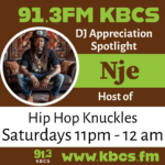Nje sitting on couch in back shirt and jeans - KBCS DJ logo brown and green with text