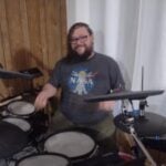 John Weir, bearded guy with glasses in a grey NASA Tshirt sitting behind drum kit