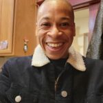 Smiley face of man in blue black denim jack with plush white collar in front of door and cabinet