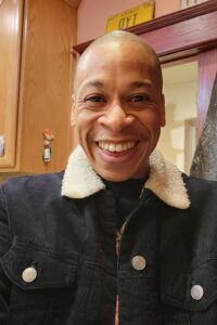 Smiley face of man in blue black denim jack with plush white collar in front of door and cabinet