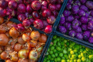 Brightly colored onions and vegetables in crates at a farmer's market.