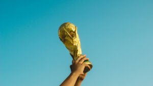 Gold World Cup trophy raised in the air with bright blue sky in the background.