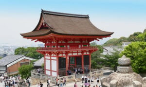 White Japanese temple with red trim to structure with tourists visiting the site.