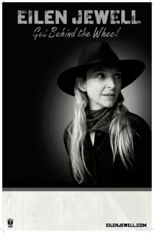 Black and white promotional poster for Eilen Jewell's album Get Behind the Wheel featuring a woman in a wide brim hat and patterned scarf looking off to the side against a dark moody background with the album title in cursive script below her name
