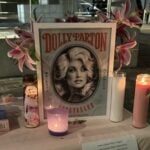 Printed photograph of Dolly Parton with pink and white candles and flowers on a table.