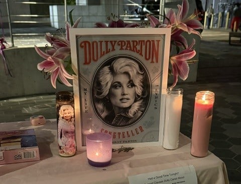 Printed photograph of Dolly Parton with pink and white candles and flowers on a table.