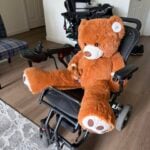 Large brown teddy bear sits in wheelchair in an apartment.